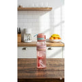 Pink water bottle with blue straw on a wooden table in a kitchen.