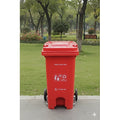 Red trash bin with recycling symbols in a park setting