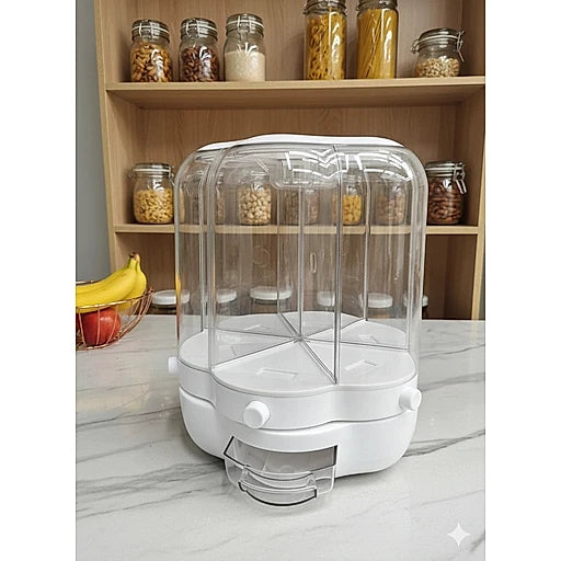 A white and clear plastic multi-compartment food storage container with a transparent dome lid, placed on a marble countertop in front of wooden shelves filled with jars of pasta and grains.