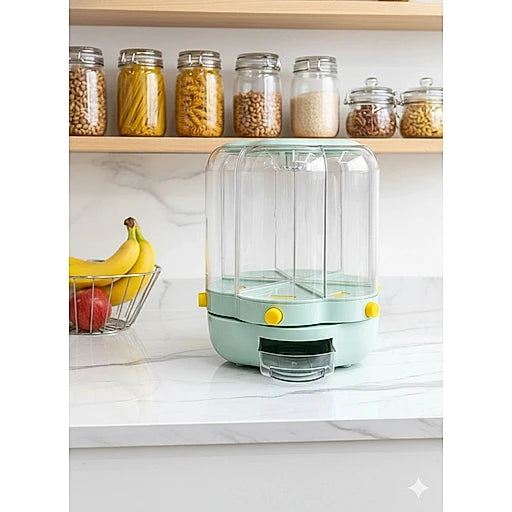 A mint green and clear plastic food storage container with yellow accents sits on a white marble countertop in a kitchen setting, with bananas and jars of pasta visible in the background.