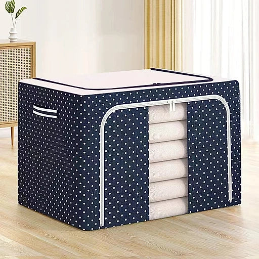 Navy blue storage cube with white polka dots containing folded white clothes on a wooden floor.